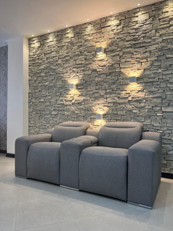 Sofá Relax de 2 puestos gris de Tufá Muebles frente a muro de piedra